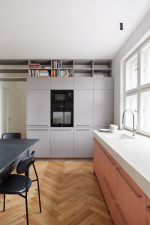 Hravost materiálu kulminuje v hlavním obytném prostoru, kde se tyrkysová vestavěná skříň v obývací části potkává s narůžovělými dvířky kuchyně z mořeného javoru. (Flexibilní rekonstrukce pražského bytu; Markéta Bromová architekti)