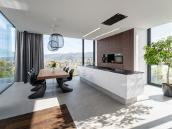 Obytná zóna navazuje na kuchyň s ostrůvkem a jídelní část, které dominuje stůl s atypickým proskleným podnožím. (Vila u Prahy, boq architekti)