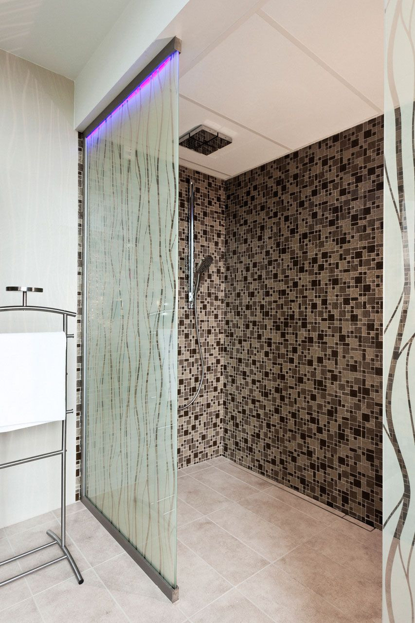 Celoskleněné fixní stěny kotvené v liště s LED pásky, materiál Grafosklo - imitace pískování, velikost 1 × 2,3 m; LED pásky v kotvící liště fixní celoskleněné stěny. Celoskleněné stěny ve sprchových koutech o velikostech 1 × 2,3 m oddělují tzv. ledopád od vlastní sprchy. Kotvící lišty byly zvoleny v širších rozměrech, aby zde mohly být současně instalovány i LED pásky, které zajišťují atypické osvětlení daného prostoru - foto