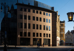 Cestou k ikonické radnici se zastavte u komerční banky. Materiálové řešení vychází z trendu nastupující postmoderny počátku 90. let, kdy byl u staveb bank a hotelů v oblibě umělý kámen, sklo a ocel.