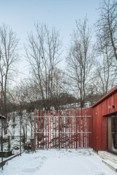 Chata v Sušici, BYRÓ architekti: Celá hmota chaty je obložená nehoblovanými střešními latěmi, ty se od sebe v místě plotu postupně oddalují a formují plot