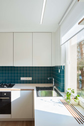 Pohled do kuchyně, která je stejně jako většina vybavení bílá. Barevný akcent vnáší zelený obklad. (Panelákový byt na Jarově, Kateřina Hodková a Markéta Smrčková)