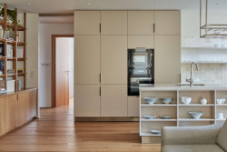 Dubovou podlahu a knihovnu doplňuje kuchyně v šedobéžovém odstínu. (Rekonstrukce bytu ve Strašnicích, MENU architekti)