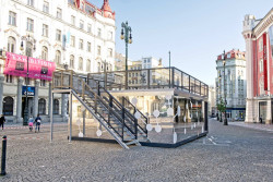 Výrazný prvek charitativní kavárny POTMĚ představuje zrcadlová fasáda z kompozitních hliníkových panelů albond, které odráží své okolí a kavárna se tak stává symbolicky neviditelnou.