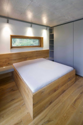 Hlavní ložnice se nachází v přízemí. Je schovaná za schodišťovou zdí. (Chata v Posázaví, Studio Sporadical)