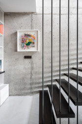 Jedním z nevýraznějších prvků bytu je zavěšené schodiště, které se vine obývacím pokojem podél stěny z ocelových prutů. (Interiér třípodlažního bytu v Praze od studia OOOX)