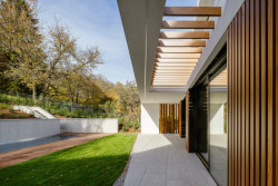 Severní terasa domu odstíněná přesahy vnějších zkosených dispozic a dřevěnými lamelami  (Block House v Šáreckém údolí v Praze; Studio MA)