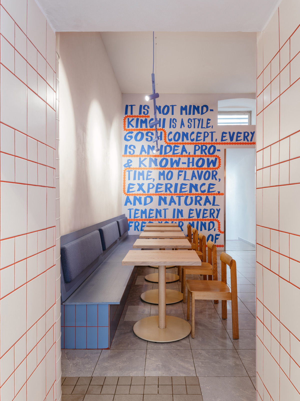 Kontrast k modré vytvářejí červené spáry bílých obkladů a oranžová mříž nad výdejním pultem. (The Kimchi; SOA architekti)