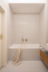 Bílý mozaikový obklad, oblé rohy a rozptýlené světlo navozují pocit lázeňství. (rekonstrukce prvorepublikového bytu v Bubenči, Studio COSMO)