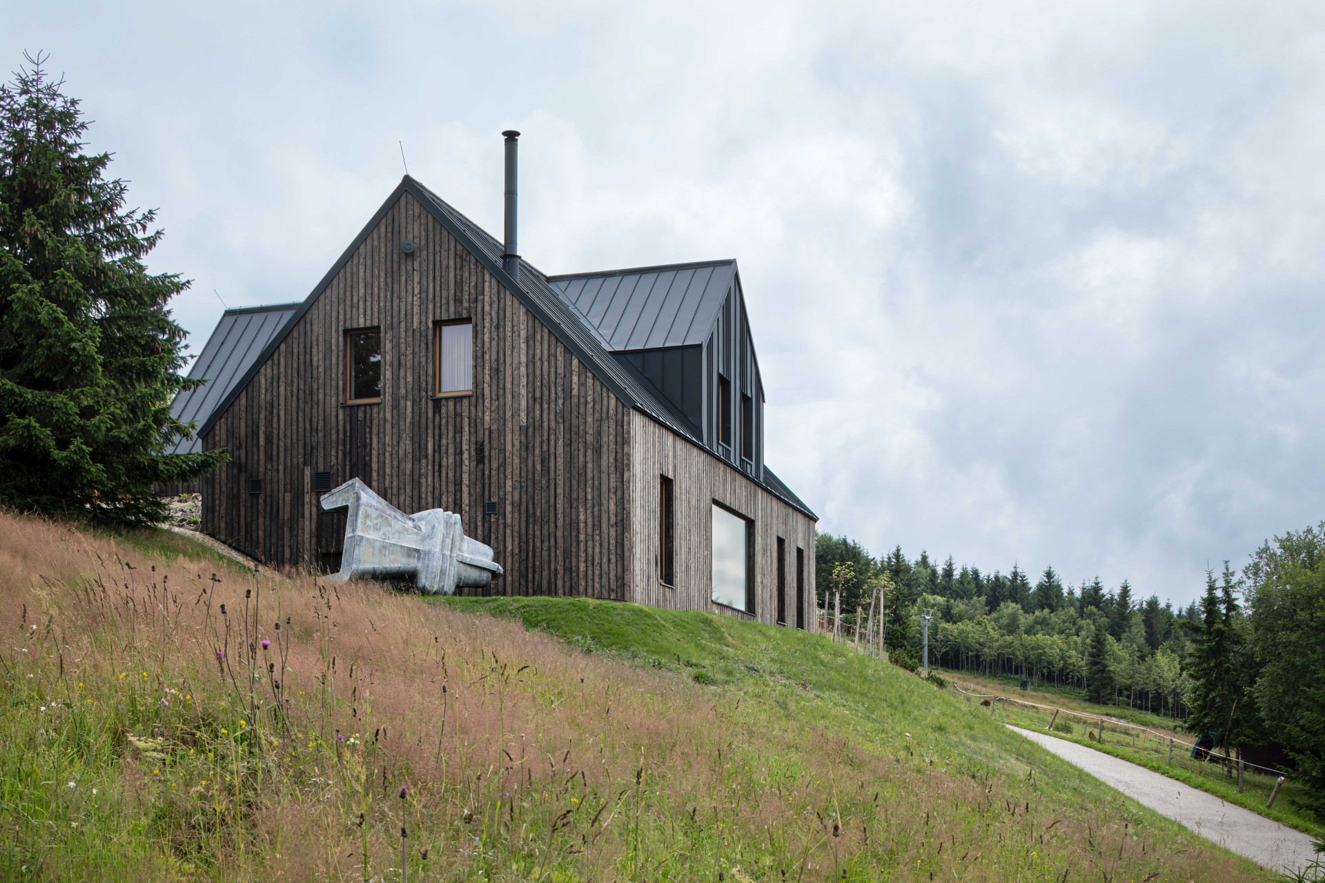 Na zahradě jim leží kovová socha, kterou si můžou prohlédnout kolemjdoucí. (OK PLAN ARCHITECTS, Rodinná bouda)