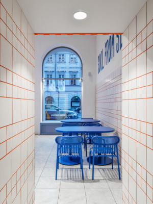 Kontrast k modré vytvářejí červené spáry bílých obkladů a oranžová mříž nad výdejním pultem. (The Kimchi; SOA architekti)