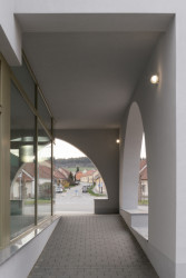 Podloubím prochází veřejný chodník, který v případě nepřízně počasí poskytuje úkryt jak před sluncem, tak i před deštěm. (Sokolovna ve Veverských Knínicích, studio New Work)