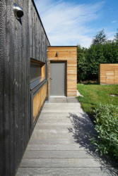 Novostavba má fasádu ze dřeva, kde se kombinují pálená prkna a přírodní dřevěné latě. (Chata v Posázaví, Studio Sporadical)