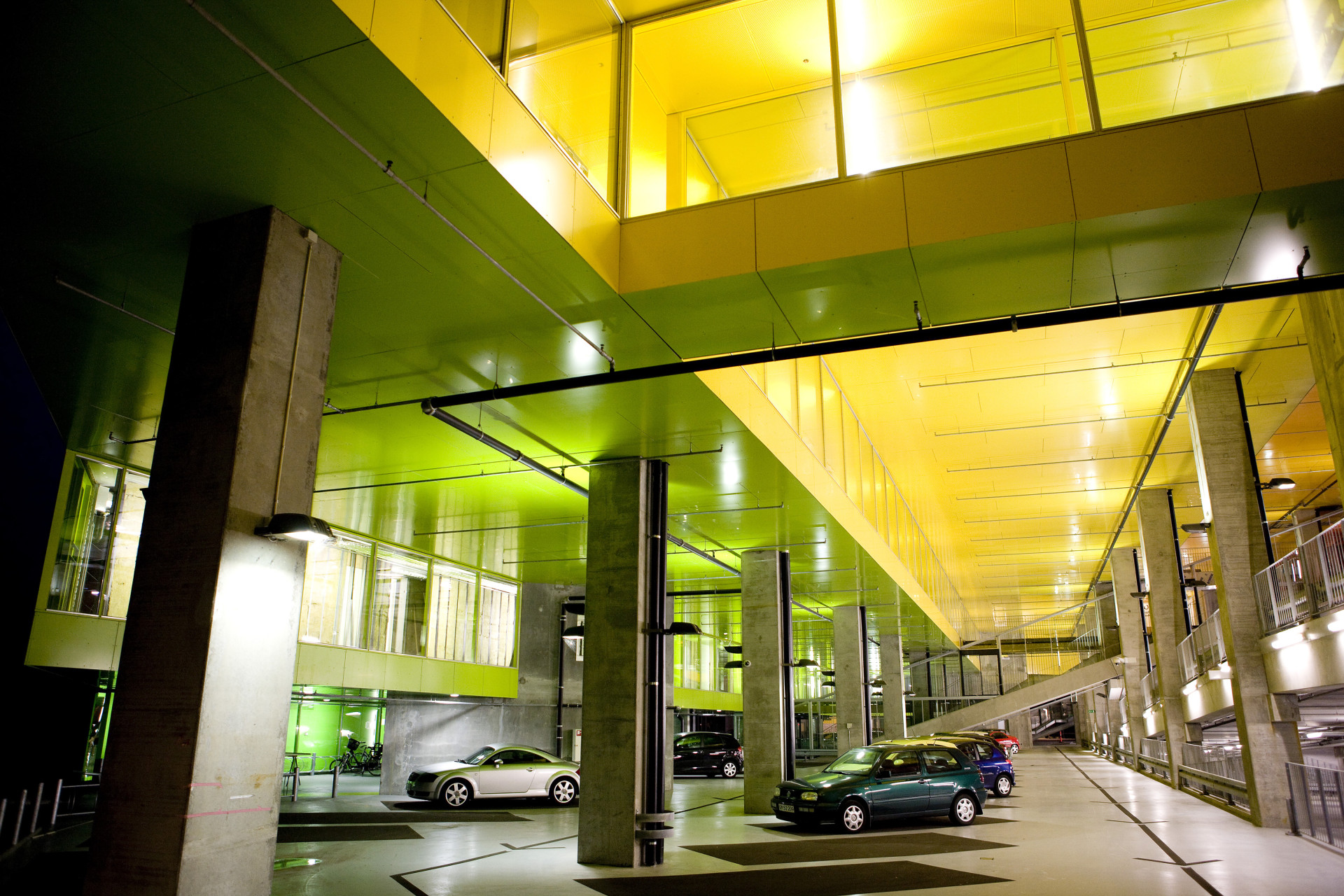 Kontrast mezi dřevem obloženými, do zeleně zahalenými jednotkami pro bydlení a prostorově členitými barevnými garážemi je výrazný. 