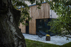 Rodinný dům v Písnici, daviddavidová architekti: Přístavba je opláštěná dřevěným, vertikálně kladeným obkladem z nehoblovaných a neošetřených modřínových prken