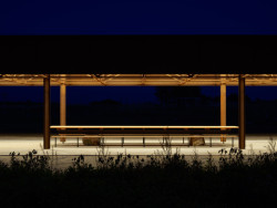 Čtvrtá strana je otevřená a chráněná plechovou střechou, pod kterou je umístěn dlouhý dřevěný stůl s dvěma lavicemi. (Zahrada Hage, Brendeland & Kristoffersen)