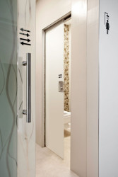 Celoskleněné dveře posuvné do pouzdra bez obložky, materiál Grafosklo – mléčná folie, velikost standardní; Bezobložkové stavební pouzdro pro zasouvací dveře. V rámci potřeby úspory místa, byly použity v sociálním zázemí toalet zasouvací dveře do stavebního pouzdra. Pro zachování designové čistoty prostoru byl zvolen bezobložkový typ stavebního pouzdra – POUZDRO AKTIVE STANDARD. To je zabudováváno do stavby ve fázi hrubé stavby a při jeho dokončování k hraně průchozího otvoru je nutné použít speciální tmel, abychom zabránili budoucímu praskání nápoje vnitřní zárubně a vlastní příčky - foto