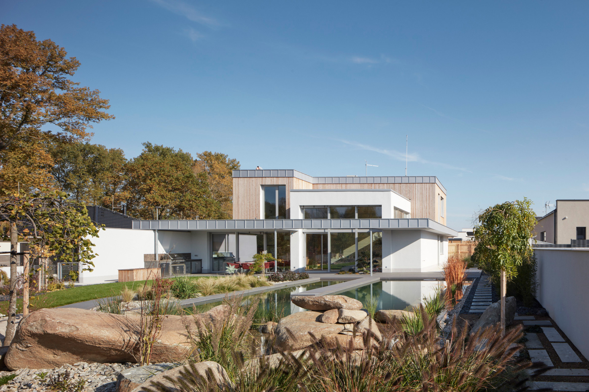 Rodinný dům u Pardubic, 0,5 Studio: Dům má silně horizontální charakter, umocněný především předstupující římsou střechy s oplechováním, která jako výrazná linka tvoří předěl mezi přízemím v bílé omítce a prvním patrem s dřevěným obkladem