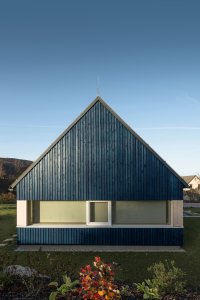 Chata v Jizerských horách, Markéta Cajthamlová, Architektonická projekční kancelář: Sokl domu je ze světlého pohledového betonu, fasáda pak z vertikálně kladeného prkenného obkladu v tmavě modré barvě