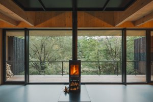 Dominantou obytného prostoru jsou krbová kamna. (Chata u Sázavy mezi skálou a řekou; Mimosa Architekti)