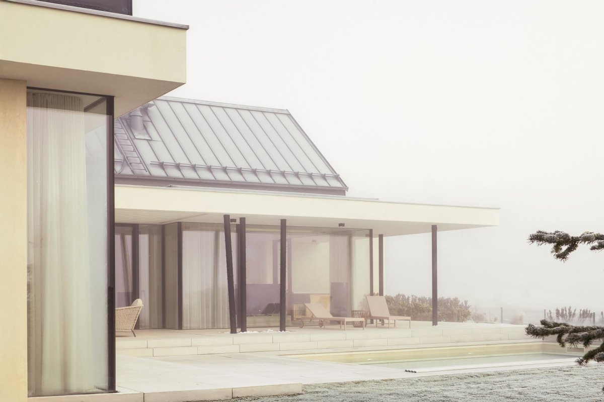 Černé subtilní rámy prosklených exteriérových stěn a štíhlé nosné sloupy dodávají stavbě jemnou dynamiku a elegantní kontrast k přírodním tónům fasády a okolní zahrady. (Bungalov ve východních Čechách; Atelier Kunc)
