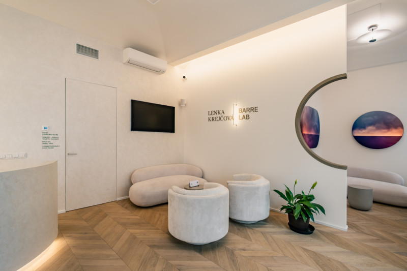 Recepční a relaxační část studia s oblými liniemi, jemnou barevností a dubovou podlahou pokládanou do vzoru chevron. (Barre Lab; Barbora Hrtáňová)