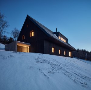 Tvaroslovím se snaží zapadnout mezi okolní stavby. Má sedlovou střechu a obdélníkový půdorys. Obložená je dřevem. (Chalupa Milada, studio ADR)