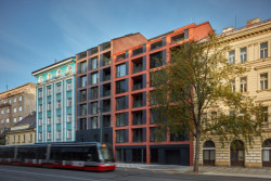 Keramický obklad zbylé fasády sice podporuje charakter industriálních budov, nicméně v posledním nadzemním podlaží plynule přechází ze svislé fasády do střešní roviny, díky čemuž projev domu působí současně. (Bytový dům Iconik, studio Edit!)