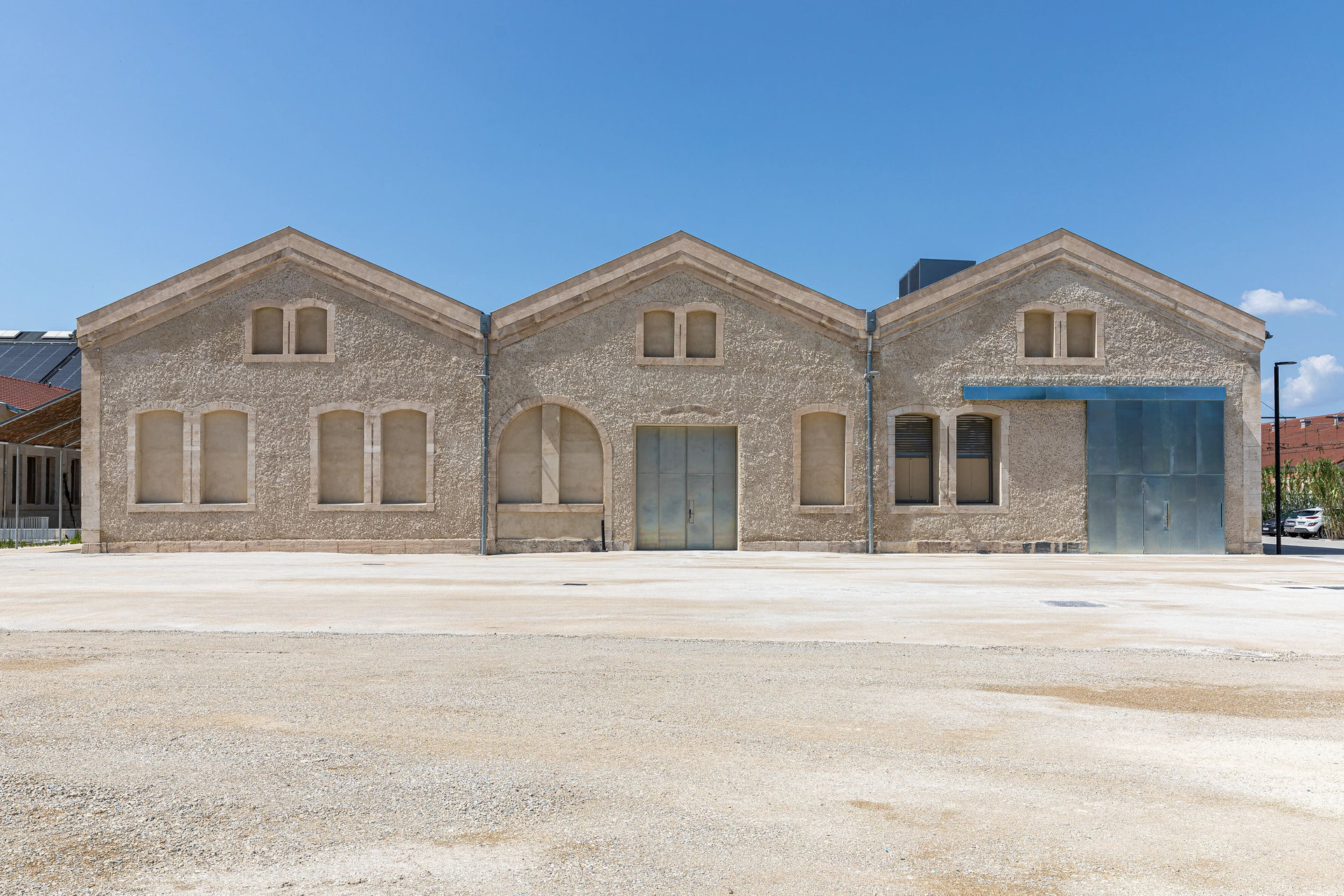 Průčelí dílen s jemnou strukturou hliněné omítky. (Rekonstrukce bývalých železničních dílen; ASSEMBLE, Atelier Luma, BC Architects )