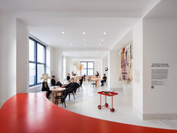 Hned vedle vstupních dveří je umístěn zaoblený sytě červený bar, který funguje jako malá kavárna. (ATLAS, No Architects)