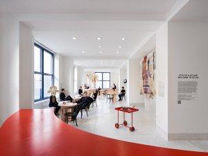 Hned vedle vstupních dveří je umístěn zaoblený sytě červený bar, který funguje jako malá kavárna. (ATLAS, No Architects)