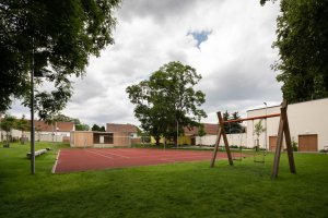 SOKEC v Hrušovanech u Brna, caraa.cz/Atelier KAVA: V zahradě je červená víceúčelová sportovní plocha, a taky klubovna, která zároveň slouží jako tribuna/jeviště/místo pro promítání