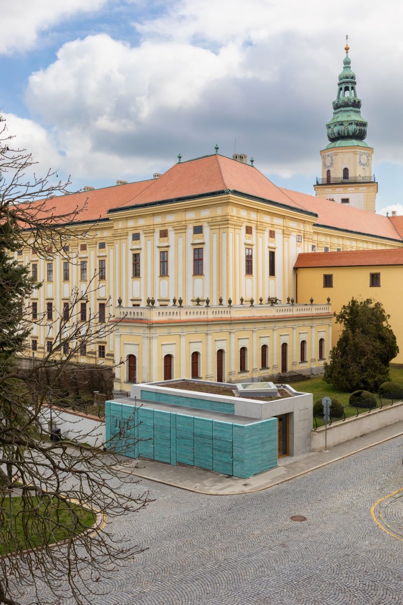 Stavba stojí v místě křížení dvou ulic, hned vedle arcibiskupského zámku a přímo v historickém centru Kroměříže. (Vstupní objekt do zámeckých sklepů s trafostanicí v Kroměříži od Atelier Štěpán)