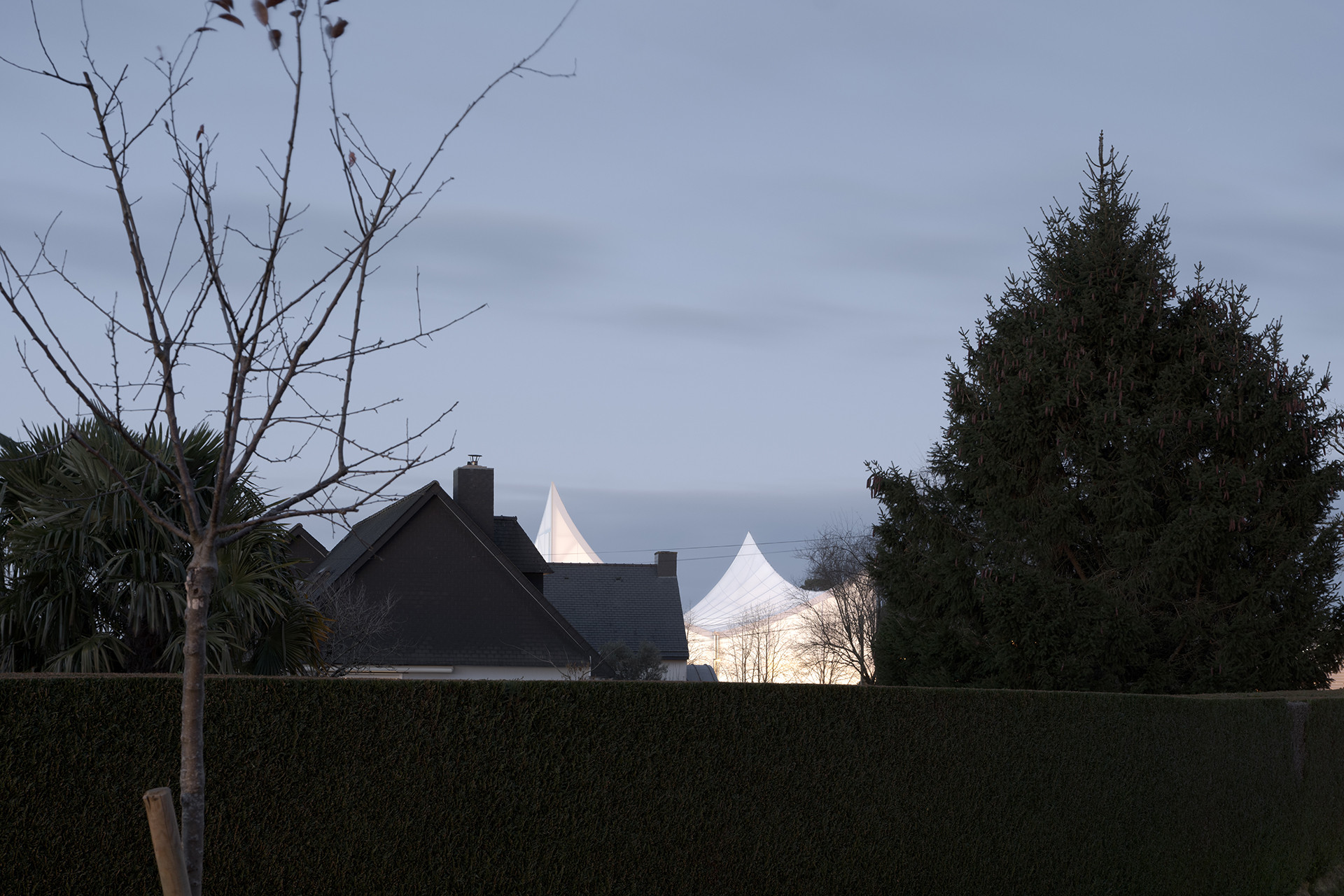 V noci bílý textilní plášť fasády svítí do dálky. (Sportovní a kulturní centrum Marie-Jose Perec a Josephine Baker v La Bouëxière ve Francii; onze04)