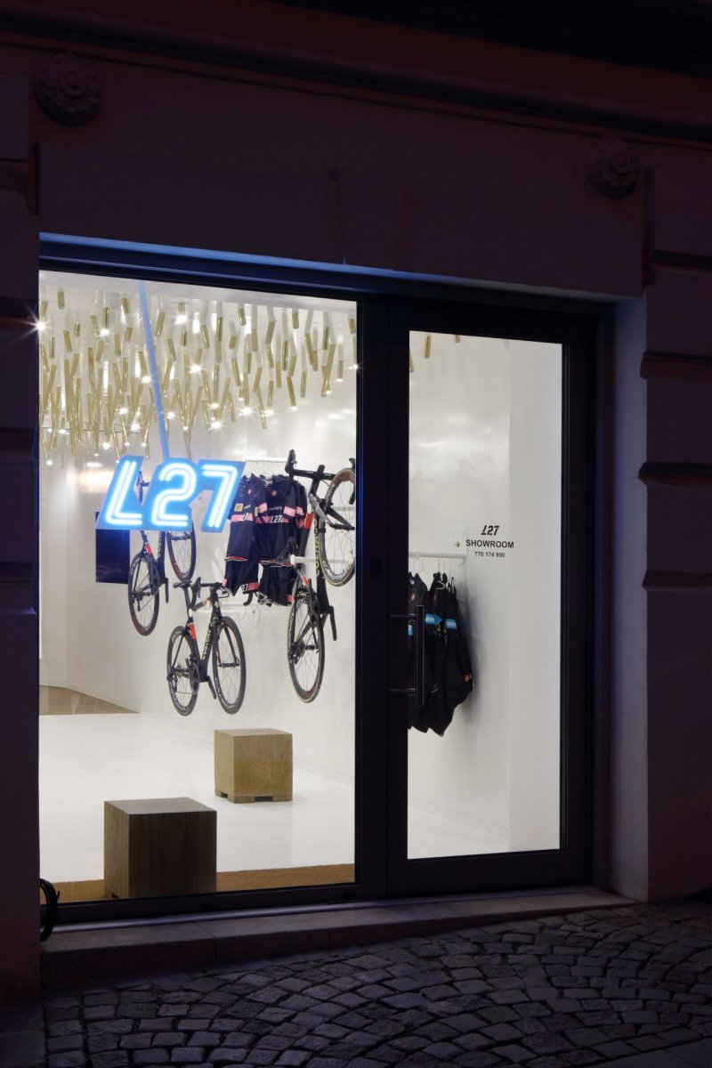 Cyklobutik L27, P6PA+Architects: Na prodejnu upozorňuje nejen bílý lesklý interiér, ale i neonový nápis umístěný do výlohy