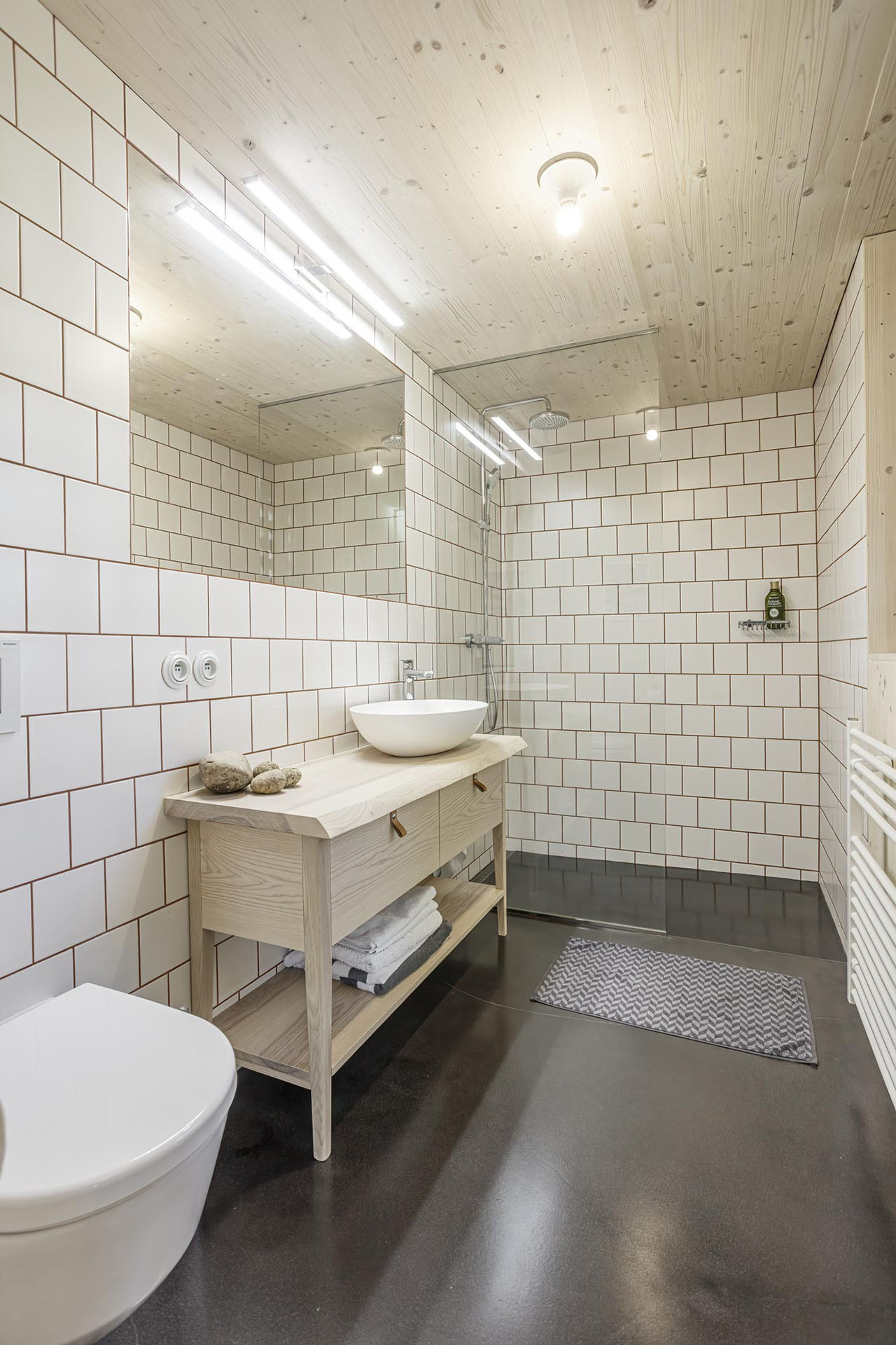 Koupelna je navržená minimalisticky. Dominuje tu bílá barva v kombinaci s dřevem. (Chata v Kořenově, Facha architekti)