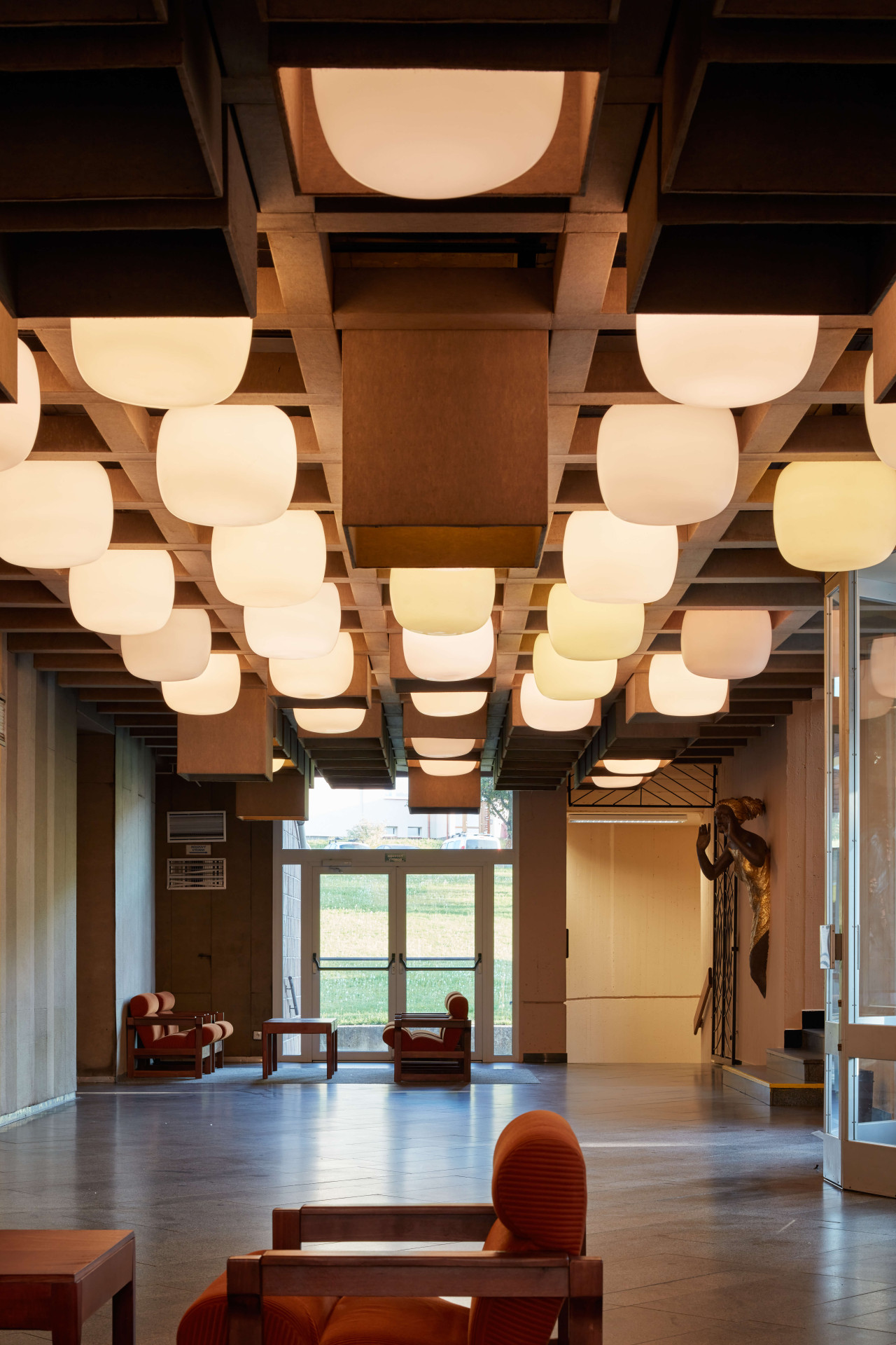 Nejkrásnějším prostorem březnického kulturáku je jednoznačně vstupní hala, které dominuje plasticky rozehraný rastr podhledu, ze kterého vystupují velká skleněná svítidla. 