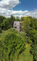 Rodinný dům je obklopený zelení. Stojí na svažitém pozemku nedaleko lesa a potoka. (Chata JARO u Prahy, edit! architects)