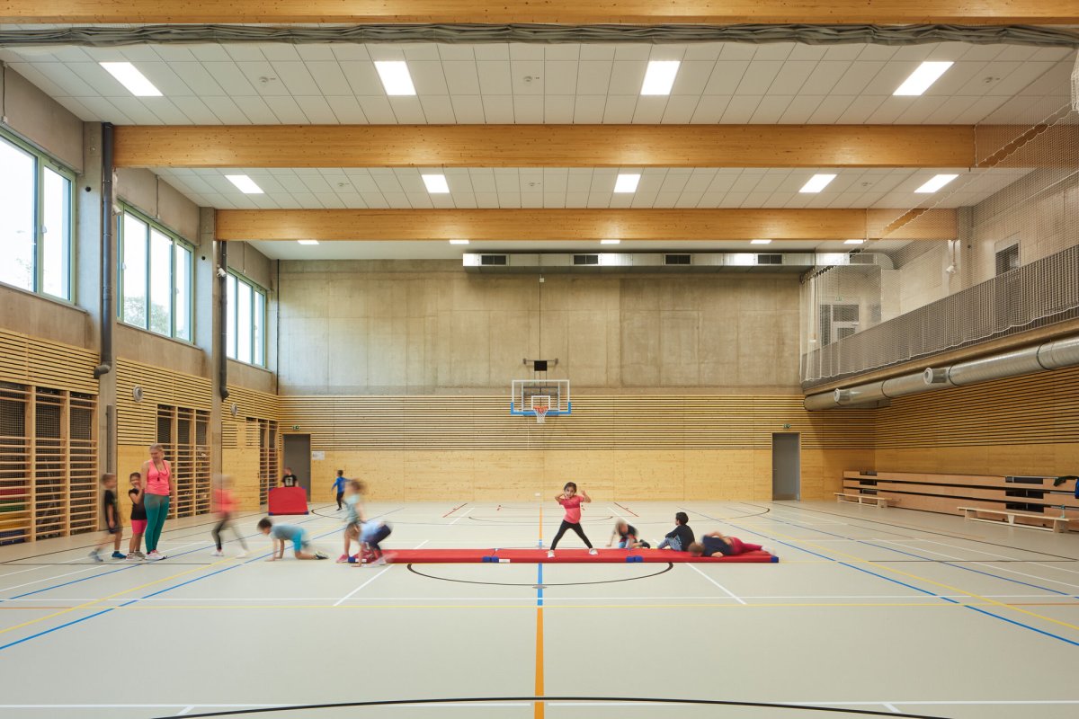 V tělocvičně dominují dřevěné prvky, pohledový beton a šedá podlaha s barevnými čárami pro různé sporty. (ZŠ bratří Fričů v Ondřejově; ATELIER 6)