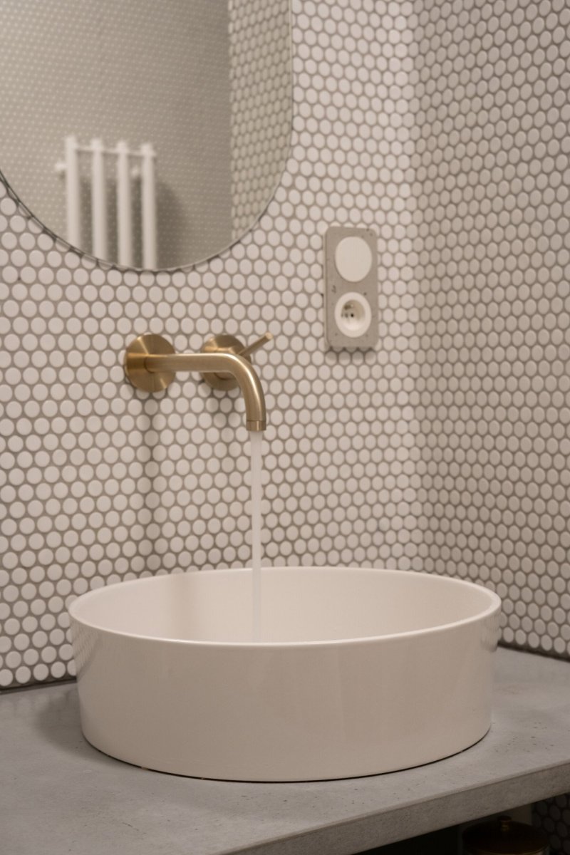 Bílý obklad doplňují mosazné baterie a niky s betonovými deskami. (rekonstrukce prvorepublikového bytu v Bubenči, Studio COSMO)