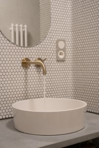 Bílý obklad doplňují mosazné baterie a niky s betonovými deskami. (rekonstrukce prvorepublikového bytu v Bubenči, Studio COSMO)