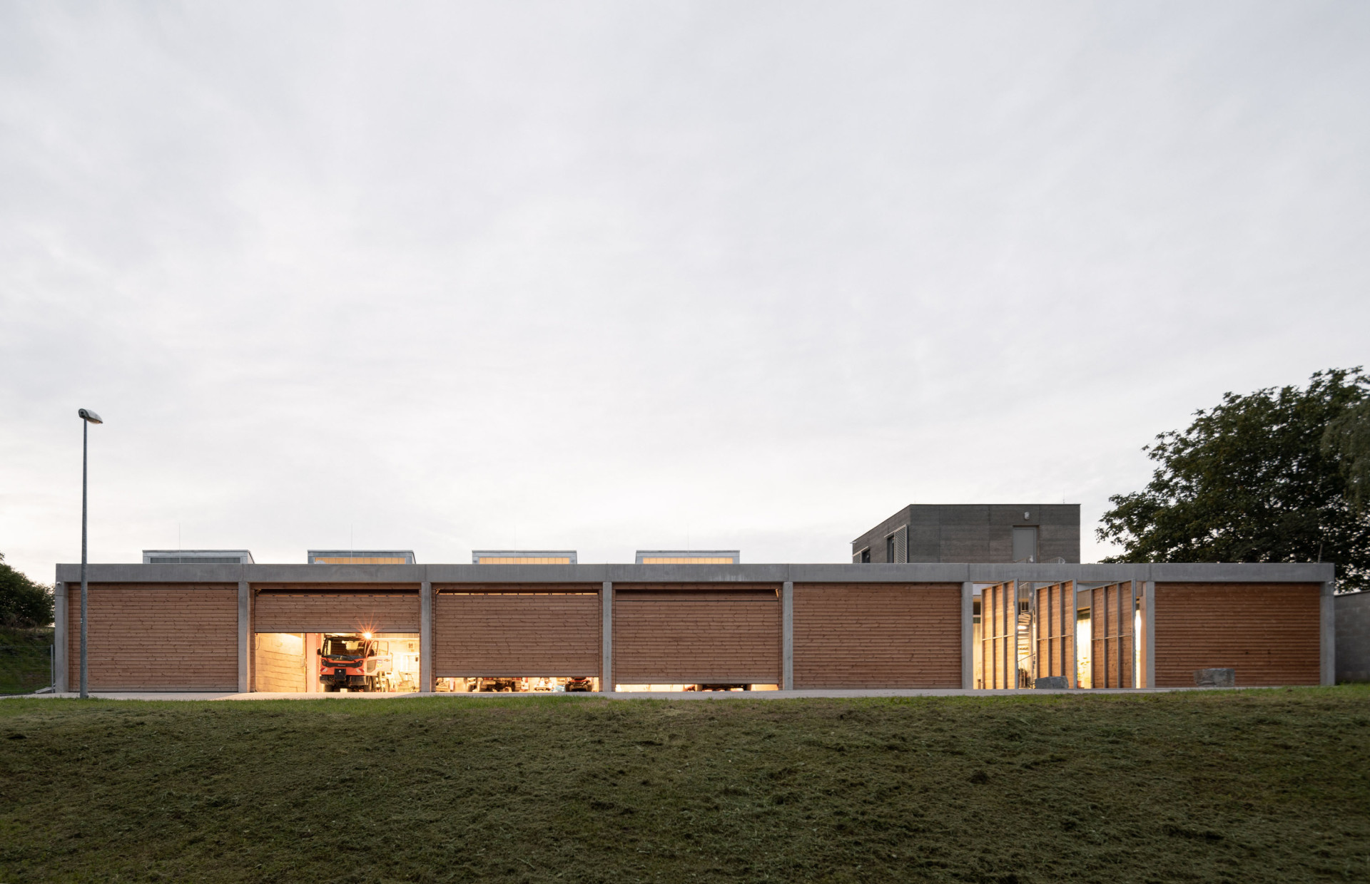 Nízký objekt základny technických služeb v Lysolajích se částečně noří do terénu, aby tak přílišně nevyčníval a současně mohl fungovat v energeticky úspornějším režimu. (Základna technických služeb, PROGRES architekti, 2022)