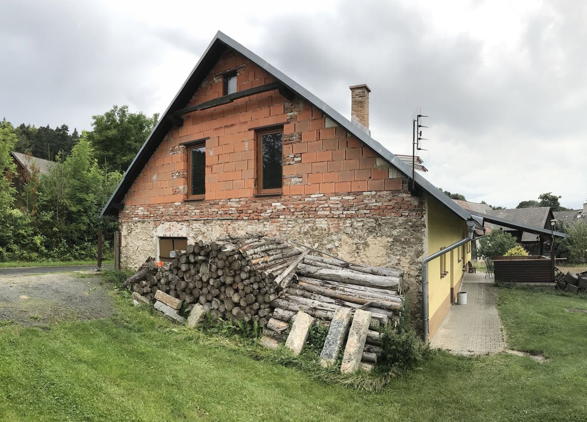Jelikož se původní rekonstrukce nikdy nedokončila a štítové stěny zůstaly bez polystyrenu, šlo vidět, že je dům do určité výšky vyzděný z kamene. (Rekonstrukce rodinného domu na Šumavě, Archport)