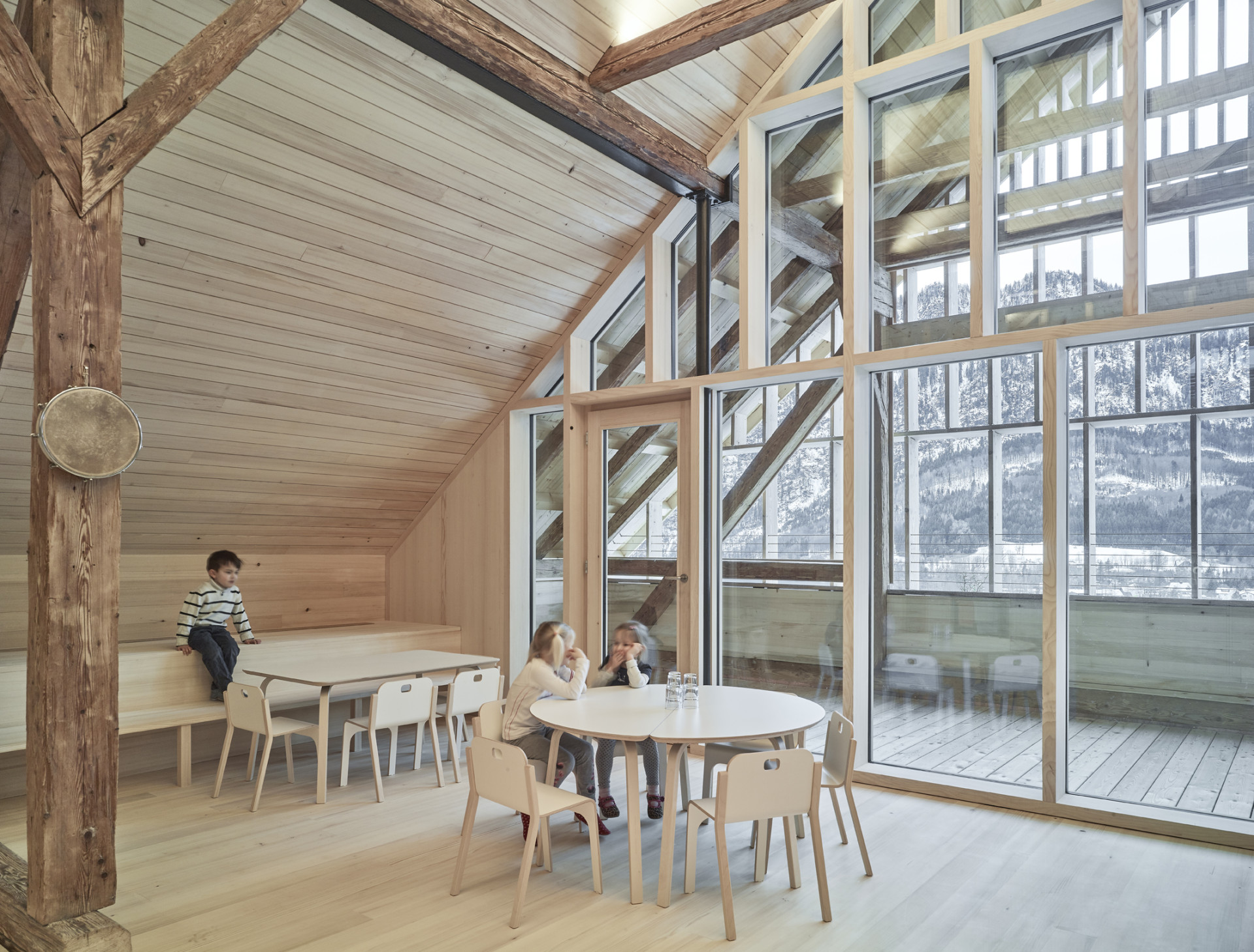 Výstavbou nové střechy vznikl velkorysý přívětivý prostor s dostatkem přirozeného světla díky prosklenému štítu. (Mateřská škola v Unterachu, Ateliér Hohengasser Wirnsberger)