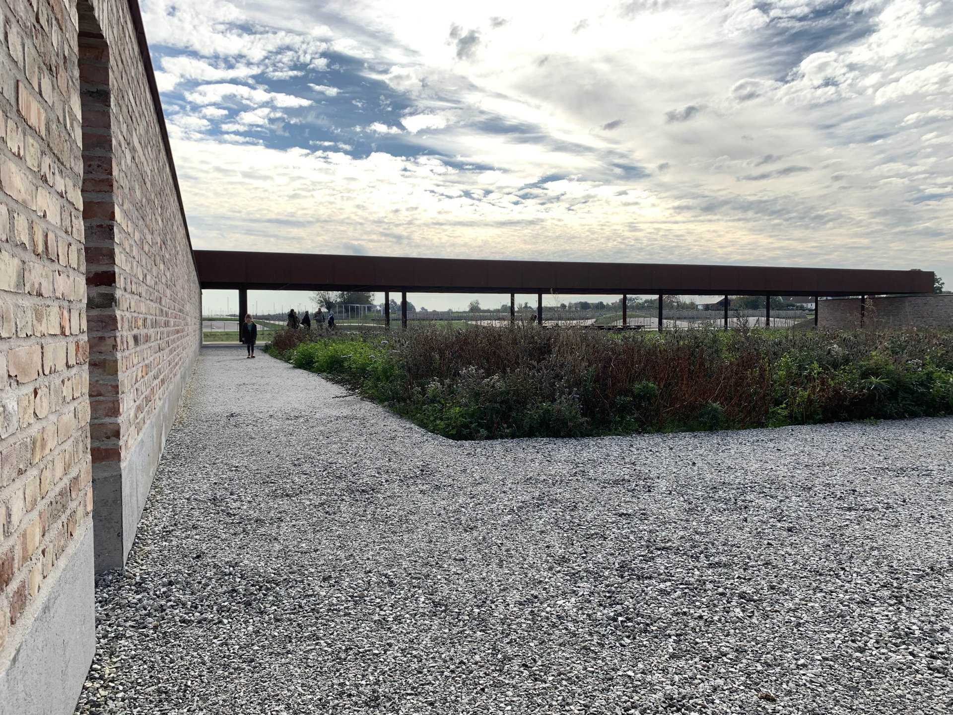 40x40 metrů. Takový je rozměr čtvercové zahrady. Tři ze čtyř stran jsou oploceny zdí. Architekti ji postavili z recyklovaných cihel, čtvrtá strana je zastřešená, pod střechou je umístěn dlouhý dřevěný stůl s dvěma lavicemi.