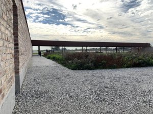 40x40 metrů. Takový je rozměr čtvercové zahrady. Tři ze čtyř stran jsou oploceny zdí. Architekti ji postavili z recyklovaných cihel, čtvrtá strana je zastřešená, pod střechou je umístěn dlouhý dřevěný stůl s dvěma lavicemi.