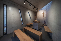 Autoři o oknech hovoří jako o zhmotnění paprsků jihozápadního slunce, které před dopadnutím na kapli filtrují blízké vzrostlé stromy. (Kaple v Praze-Záběhlicích; JIRSA – ARCHITEKTI)