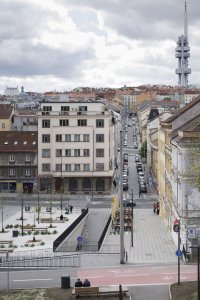Chodníky podél činžovních domů se místy rozšiřují stupňovitým sezením pro hosty přilehlých hospod a kaváren. (Tachovské náměstí v Praze, OVA)