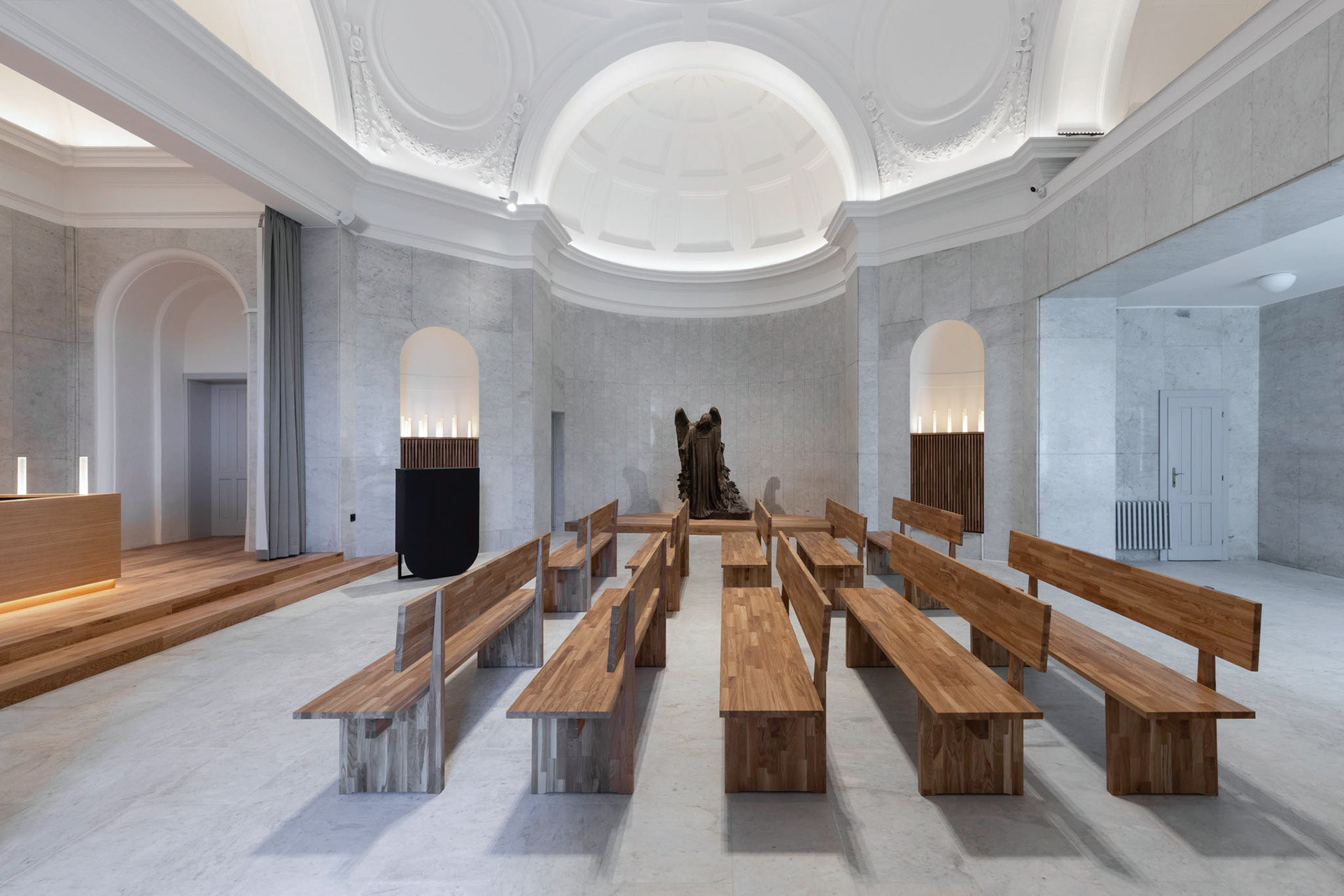 Kontrast mezi studeným kamenným obkladem a teplým dřevem (Rekonstrukce obřadní síně na Olšanských hřibitovech; Ateliér Schwestern)