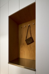 Šatní skříň spojená s botníkem kombinuje bílou barvu s bukovou překližkou v nice a nerezovým plechem na sezení. (Rekonstrukce bytu ve Vršovicích, Amulet architekti)